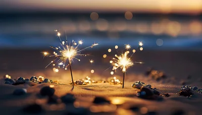 Two Burning Sparklers On A Sandy Beach At Sunset