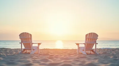 Two Empty Adirondack Chairs On A Sandy Beach At Sunset