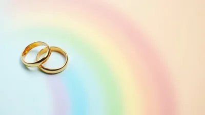 Two Gold Wedding Rings On A Pastel Rainbow Background