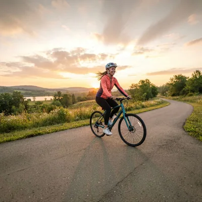 Woman Cycling On A Scenic Paved Path At Sunset
