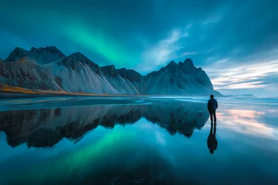 Man Standing On Reflective Beach Under Northern Lights