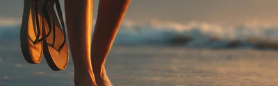 Woman Holding Flip Flops Walking Along The Beach