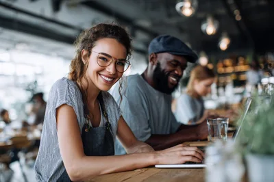 Smiling Female Barista Working On Laptop In Cafe