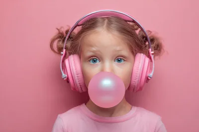 Young Girl Wearing Pink Headphones Blowing Bubblegum