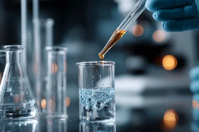 Scientist Adding Chemical Reagent To Beaker In Laboratory