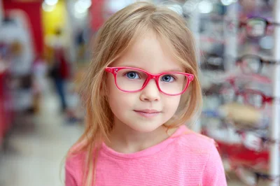 Little Girl Trying On Pink Glasses In Optical Store