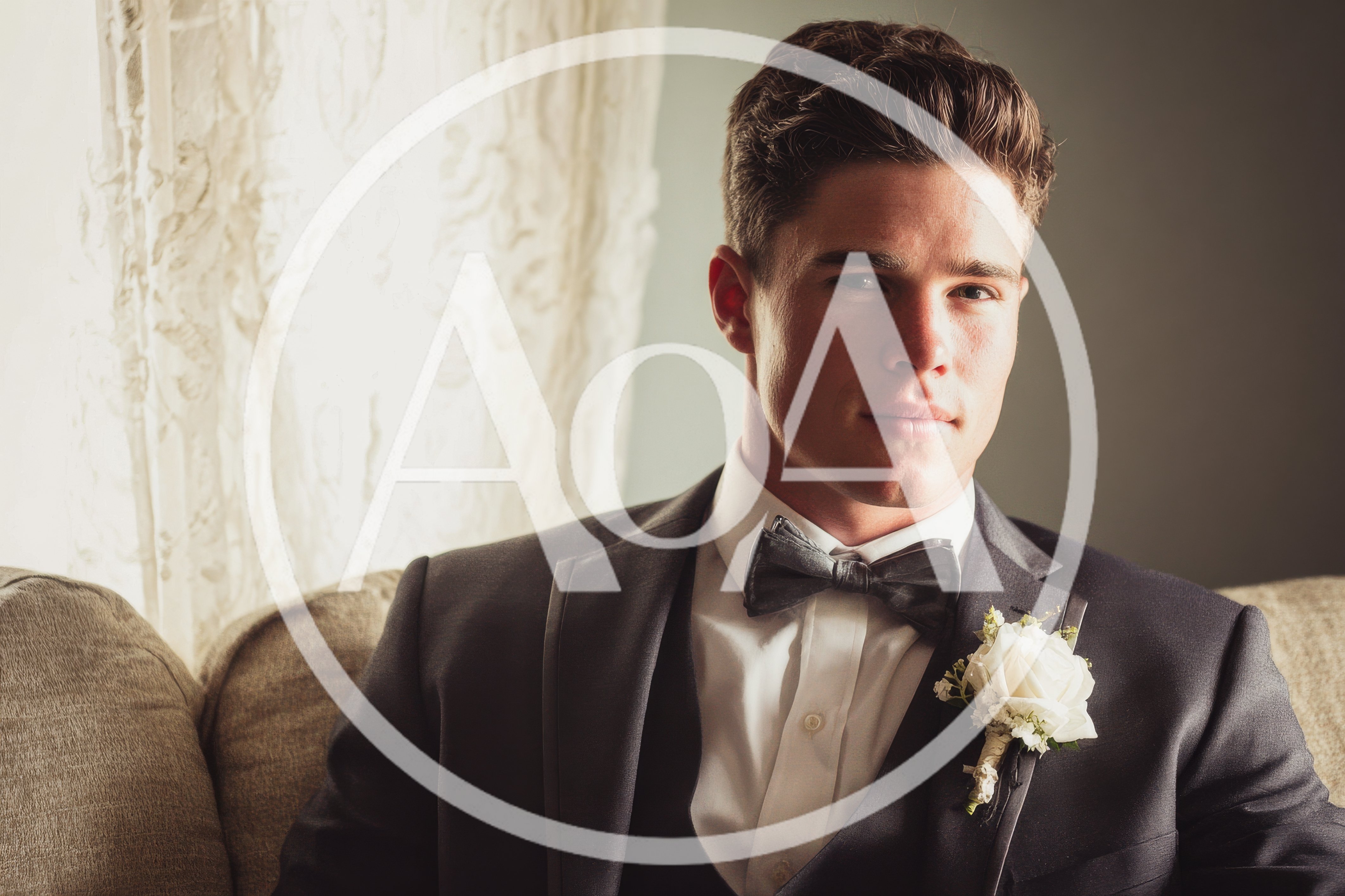 Handsome Groom Sitting On Sofa In Formal Suit