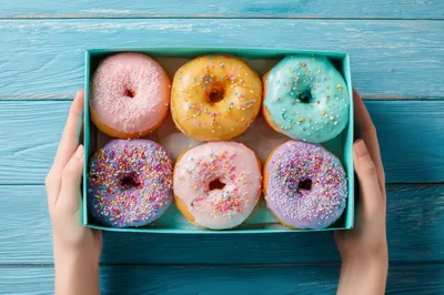 Hands Holding A Box Of Assorted Glazed Donuts
