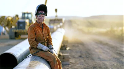 Female Welder Sitting On Industrial Pipeline At Construction Site