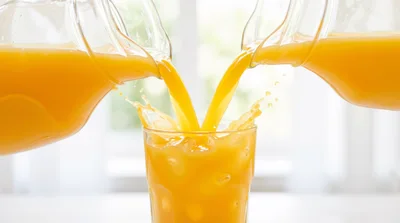 Two Pitchers Pouring Orange Juice Into A Glass
