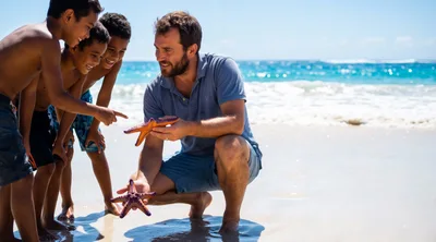 Father Showing Starfish To His Children On Beach