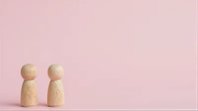 Two Wooden Peg Dolls Standing On Pink Background