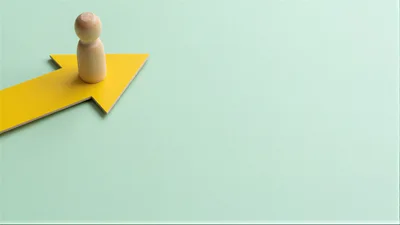 Wooden Peg Doll Standing On A Yellow Arrow