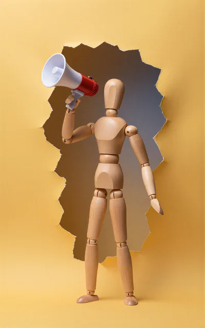Wooden Mannequin Holding A Megaphone Through Torn Paper