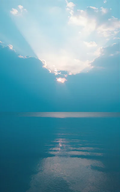 Sunlight Breaking Through Clouds Over Calm Ocean Waters