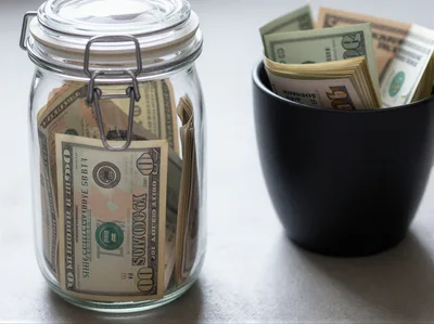 US Dollar Bills Stored In Glass Jar And Black Cup
