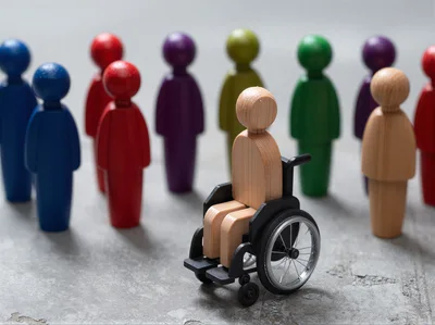 Wooden Figure in Wheelchair Surrounded by Colorful Figurines
