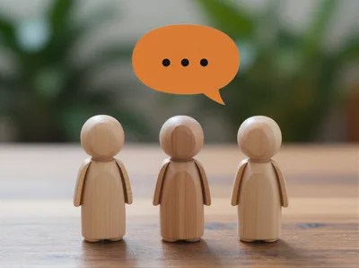 Three Wooden Peg Dolls With An Orange Speech Bubble