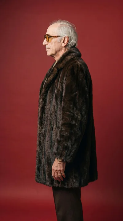 Senior Man Wearing Fur Coat Against Red Background