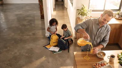 Father Pouring Orange Juice While Children Pack Backpacks