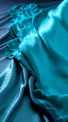 Teal Fabric Unfolding Over Purple Satin Background