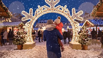 Parent Holding Child At Christmas Market Under Snowflake Arch