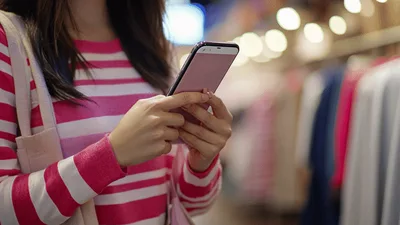 Young Woman Using Smartphone While Shopping In Clothing Store