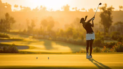 Female Golfer Putting Ball On Sunny Golf Course