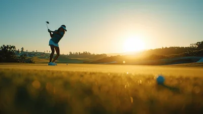 Female Golfer Swinging Club On Sunny Golf Course