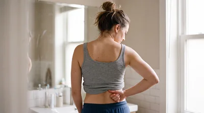 Woman Suffering From Lower Back Pain In Bathroom