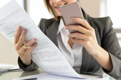 Businesswoman Scanning Document With Smartphone In Office