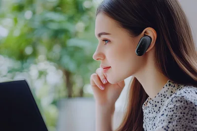 Young Woman Wearing Bluetooth Earpiece Working On Laptop