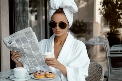 Woman in Bathrobe Reading Newspaper at Outdoor Cafe