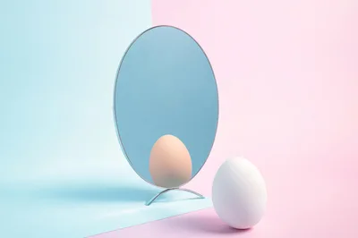 White Egg Standing Before A Round Mirror