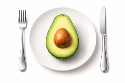 Half An Avocado On A White Plate With Cutlery