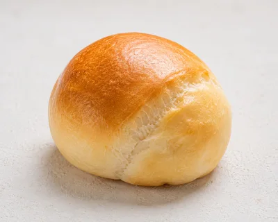 Single Golden Brown Dinner Roll on White Surface