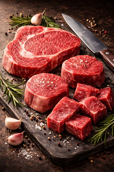 Raw Beef Steaks And Cubes On Wooden Board