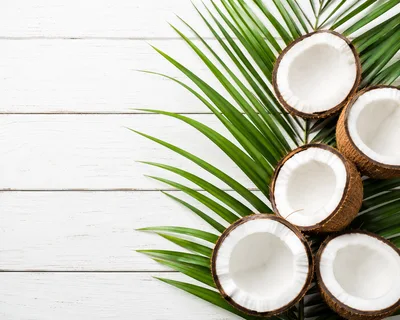 Fresh Coconut Halves On Palm Leaves And White Wood