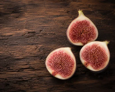 Three Halved Fresh Figs On Rustic Dark Wood