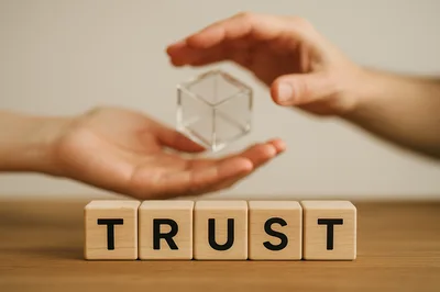 Hands Holding Transparent Cube Above Trust Wooden Blocks