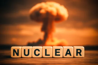 Wooden Blocks Spelling Nuclear Before A Mushroom Cloud