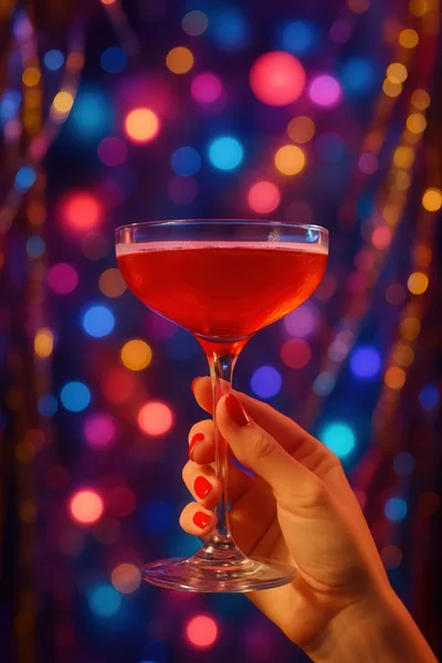 Hand Holding A Red Cocktail Glass Against Bokeh Lights