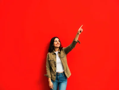Young Woman Pointing Upwards Against Red Background