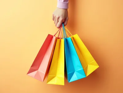 Hand Holding Colorful Shopping Bags Against Orange Background