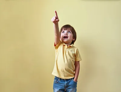 Young Boy Pointing Upwards Against Yellow Background