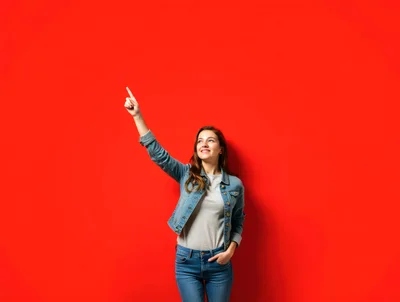 Young Woman Pointing Upwards Against Red Background