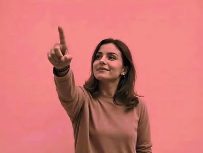 Young Woman Pointing Upwards Against Pink Background