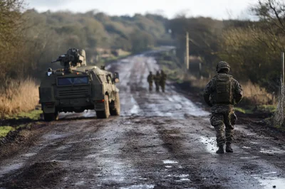 Soldier Walking Along Muddy Road With Armored Vehicle