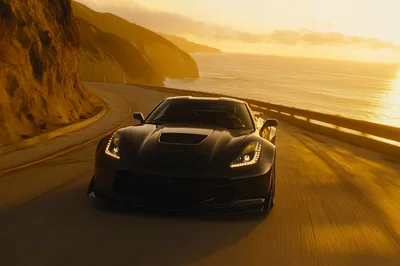 Black Sports Car Driving Along Coastal Highway At Sunset