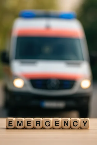 Wooden Blocks Spelling Emergency With Blurred Ambulance Background